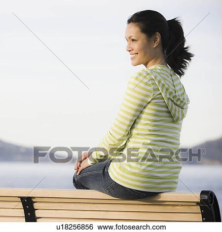 Stock Photograph - Woman relaxing on bench near sea. Fotosearch