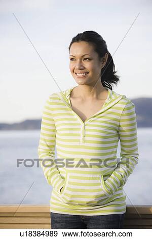 Stock Photo - "Woman standing at waterfront, smiling". Fotosearch