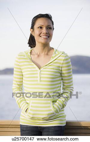 Stock Photo - "Woman standing at waterfront, smiling". Fotosearch