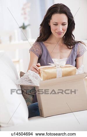 Picture - "Woman unpacking parcel with present, smiling". Fotosearch