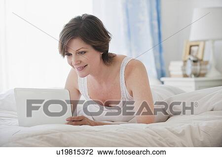 Stock Image - Woman using laptop on bed. Fotosearch