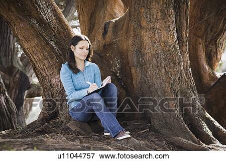 Woman writing diary by tree in park View Large Photo Image Stock Photo - Woman writing diary by tree in park. Fotosearch