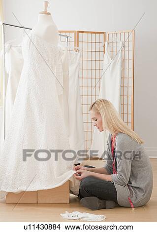 Picture - Young female tailor adjusting wedding dress in bridal shop. Fotosearch