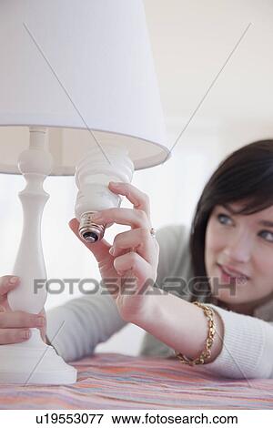 Stock Photo - Young woman changing light bulb. Fotosearch