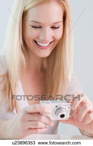 Stock Image - "Young woman reviewing photos in digital camera, smiling". Fotosearch