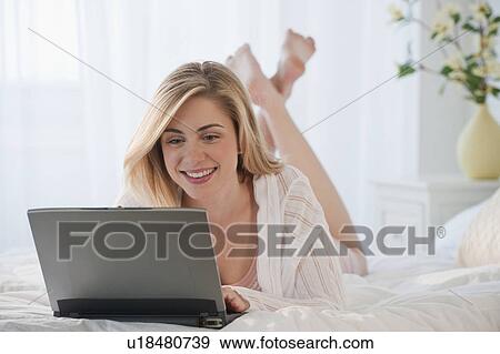 Stock Photo - Young woman using laptop on bed. Fotosearch