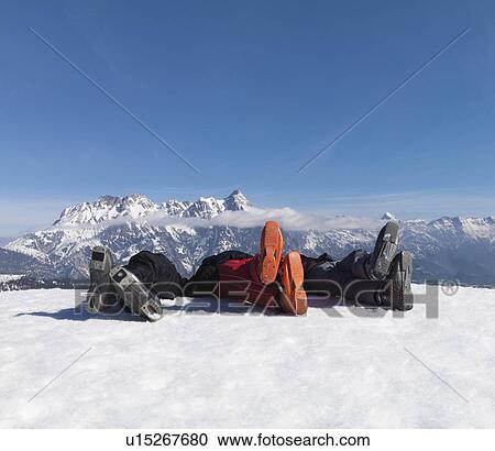 Stock Image - 3 men lying in snow on top of mountain. Fotosearch
