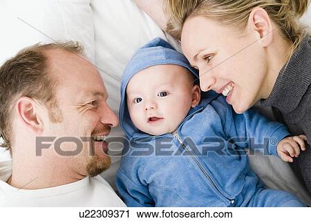 Stock Image - Baby laying between dad and mom. Fotosearch