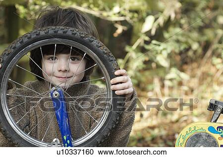 Stock Image - Boy looking through bike wheel. Fotosearch