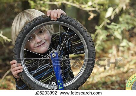 Stock Image - Boy looking through bike wheel. Fotosearch