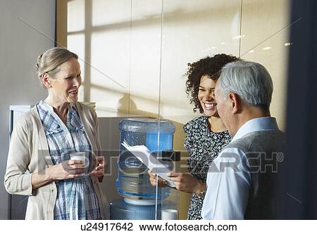 Stock Image - Casual meeting by office water cooler. Fotosearch