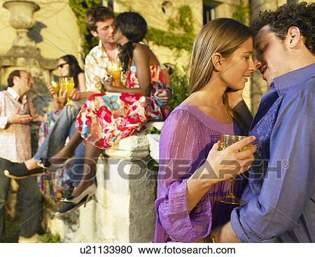 Stock Image - Couple kissing at a cocktail party. Fotosearch