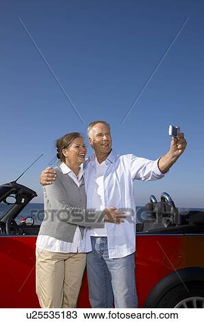 Stock Image - Couple taking photo together by car. Fotosearch