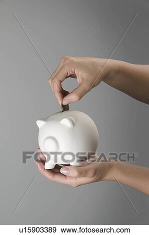 Stock Photo - Female hand placing coin in piggy bank. Fotosearch