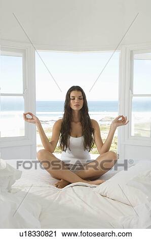 Stock Image - Female in yoga pose sitting on bed. Fotosearch