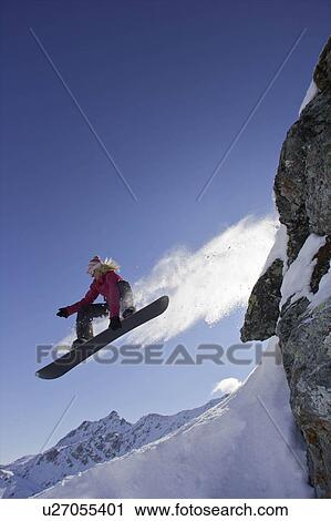 Stock Image - Female snowboarder jumping off a rock. Fotosearch