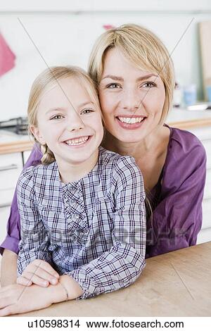 Girl and woman sitting at table hugging View Large Photo Image Picture - Girl and woman sitting at table hugging. Fotosearch