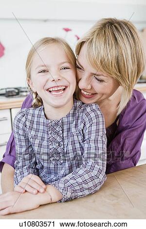 Girl and woman sitting at table hugging View Large Photo Image Stock Image - Girl and woman sitting at table hugging. Fotosearch