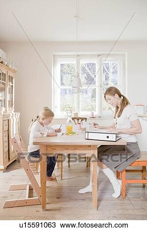 Girl and woman sitting at table writing View Large Photo Image Stock Image - Girl and woman sitting at table writing. Fotosearch