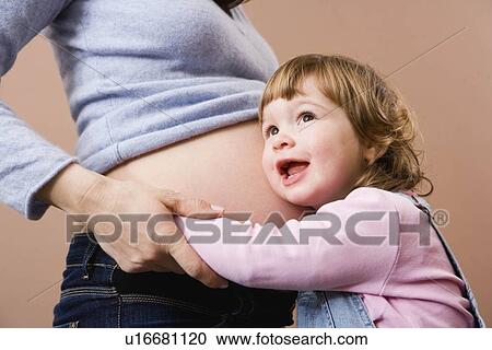 Stock Image - Girl listening at pregnant mothers belly. Fotosearch
