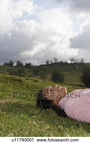 Stock Image - Girl lying on grass looking at sky. Fotosearch