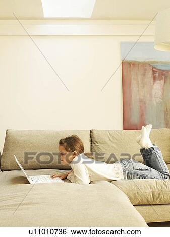 Girl lying on sofa using laptop View Large Photo Image Stock Photograph - Girl lying on sofa using laptop. Fotosearch