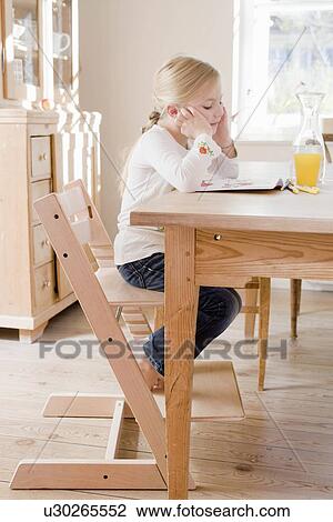 Stock Image - Girl sitting at table reading. Fotosearch