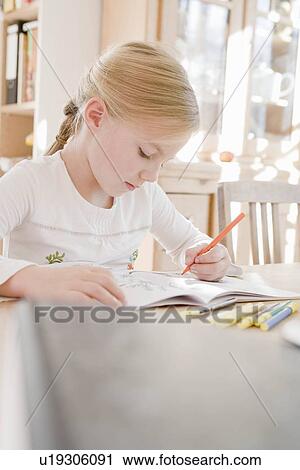Stock Image - Girl sitting at table writing. Fotosearch