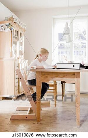 Stock Photograph - Girl sitting at table writing. Fotosearch