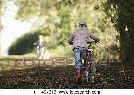 Stock Image - Girl walking bike up country lane. Fotosearch