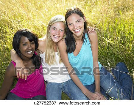 Stock Photo - "Girlfriends seated in a field, smiling". Fotosearch