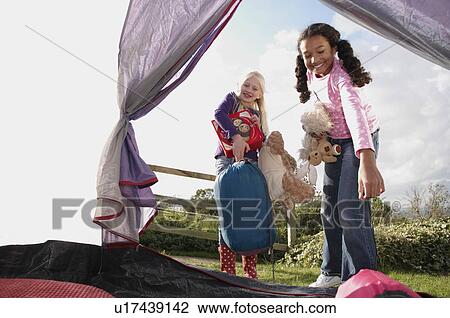 Stock Image - Girls putting sleeping bags in to tent. Fotosearch