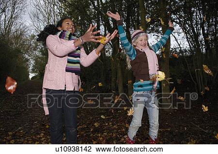 Stock Image - Girls throwing autumn leaves. Fotosearch