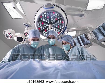 Stock Image - Group of surgeons operating in theatre. Fotosearch