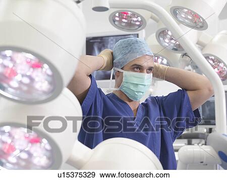 Stock Photo - Male nurse tying mask in theatre. Fotosearch