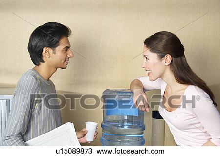 Stock Image - Man and woman chatting by water cooler. Fotosearch