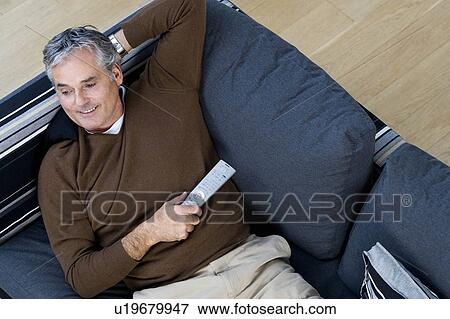 Stock Photo - Man relaxing on sofa with tv remote. Fotosearch
