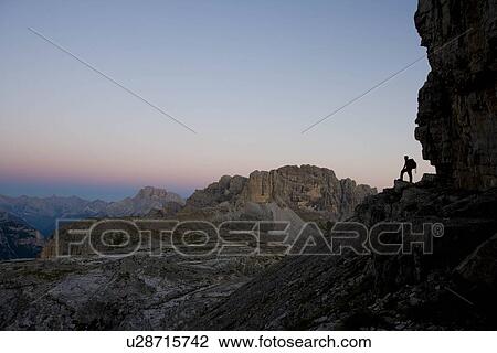Stock Image - Man standing at flank of a mountain. Fotosearch
