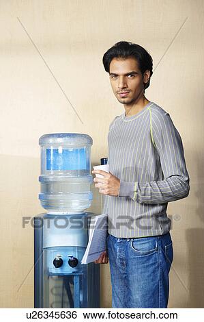 Man standing by water cooler View Large Photo Image Stock Photograph - Man standing by water cooler. Fotosearch