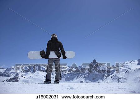 Man standing on mountain with snowboard View Large Photo Image Stock Image - Man standing on mountain with snowboard. Fotosearch
