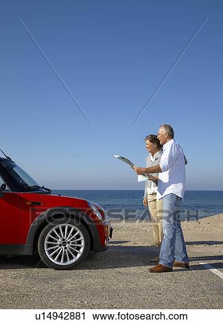 Stock Image - Mature couple looking at map by car. Fotosearch