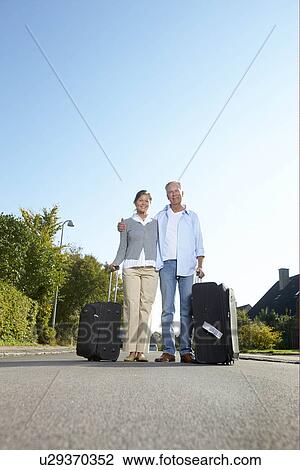 Stock Image - Mature couple with wheelie cases. Fotosearch
