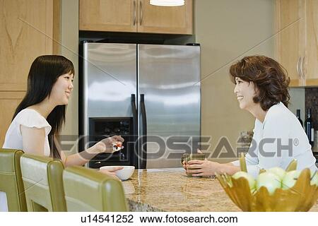 Stock Image - Mother and daughter talking in kitchen. Fotosearch