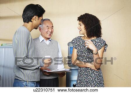 Stock Image - Office workers chatting by water cooler. Fotosearch