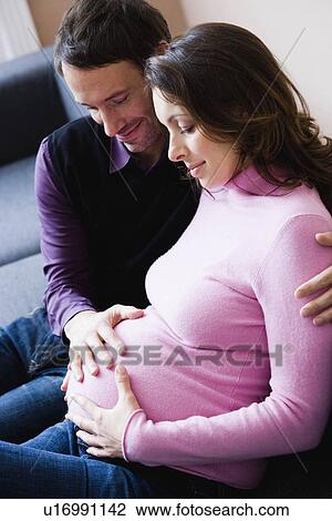 Stock Image - Pregnant woman and man sitting on couch. Fotosearch