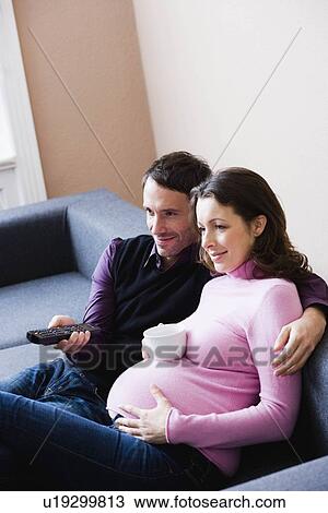 Stock Image - Pregnant woman and man sitting on couch. Fotosearch