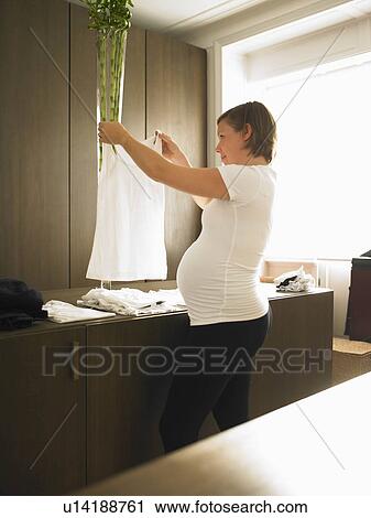 Stock Image - Pregnant woman folding laundry. Fotosearch