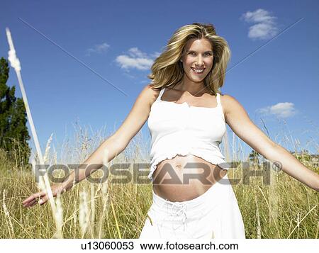 Stock Image - "Pregnant woman in a field, smiling". Fotosearch