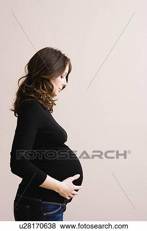 Stock Photo - Pregnant woman looking at her belly. Fotosearch