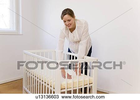 Stock Image - Pregnant woman putting together baby bed. Fotosearch